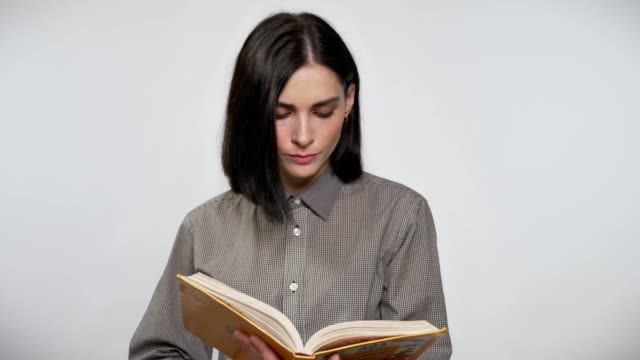 Junge-schöne-Frau-mit-kurzen-braunen-Haaren-halten-und-Buch,-konzentriert,-weißer-Hintergrund