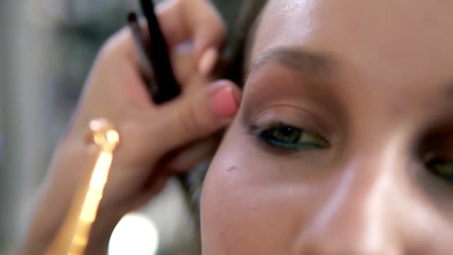 Eyes-make-up-process.-Artist-corrects-eye-line-using-a-professional-brush-with-golden-edge.-Close-up-of-a-model's-face