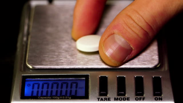 Pharmacist-puts-a-pill-on-the-scales.-Pharmacist,-weighs-the-manufactured-tablets-on-the-control-scales.-Diet-pills-on-a-scale.-Weight-loss-medicine-spilled