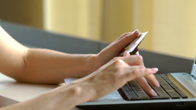 Close-up-woman's-hands-holding-a-credit-card-and-using-computer-keyboard-for-online-shopping