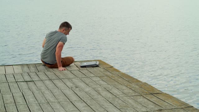 ein-Mann-nähert-sich-zum-Jahresende-ein-Mauerwerk-und-öffnen-einen-Laptop-auf-dem-Hintergrund-der-See-im-Sommer