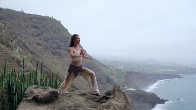 Mujer-meditando-en-pose-de-yoga-Guerrero-en-las-montañas-al-mar,-playa-y-roca.-Motivación-e-inspiración-para-montar-y-ejercicio.-Estilo-de-vida-saludable-al-aire-libre-en-la-naturaleza,-concepto-de-fitness.