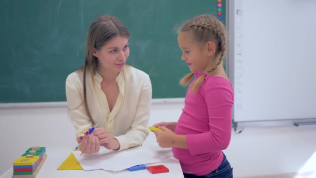 Porträt-von-glücklich-professioneller-Lehrer-weibliche-smart-Schulkind-Mädchen-mit-Kunststoff-Figuren-in-der-hand-in-der-Nähe-von-Board-im-Klassenzimmer-der-Schule