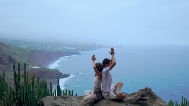 Mann-und-Frau-sitzen-auf-einem-Berg-auf-einem-Felsen-zurück-zu-meditieren-und-Yoga-auf-dem-Hintergrund-des-Ozeans-zu-tun.