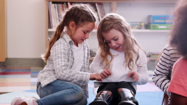 Two-elementary-school-schoolgirls-sharing-tablet-in-class