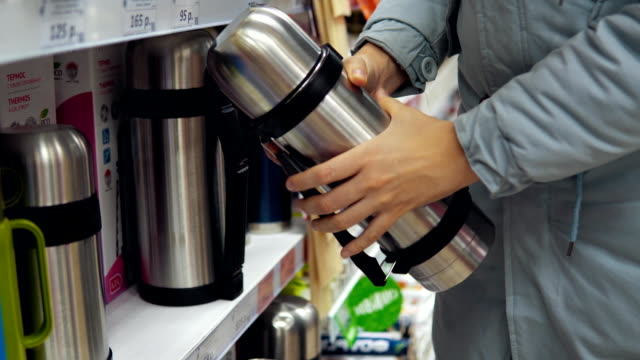 A-young-woman-chooses-a-steel-thermos-in-the-supermarket.