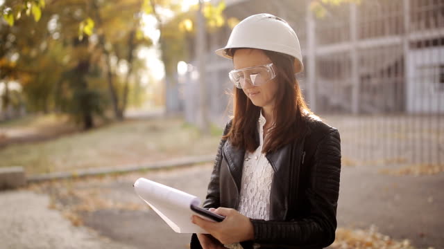 Portrait-of-young-caucasian-female-architect-standing-on-construction-site,-holding-clipboard-and-writing