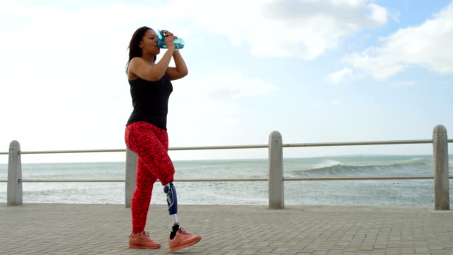 Vista-lateral-del-agua-potable-de-mujer-con-discapacidad-en-el-paseo-marítimo-4k