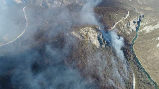 Aerial-footage-of-thick-smoke-coming-from-the-woods-with-a-road-and-a-river-next-to-the-woods