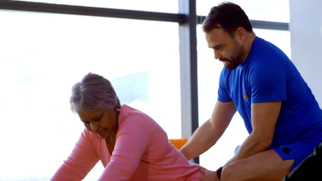 Trainer-assisting-senior-woman-in-performing-yoga-4k