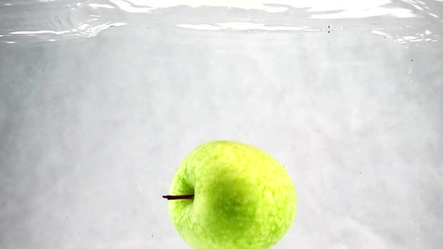 The-green-Apple-falls-into-the-water-at-a-slow-pace.-Fruits-isolated-on-a-white-background.
