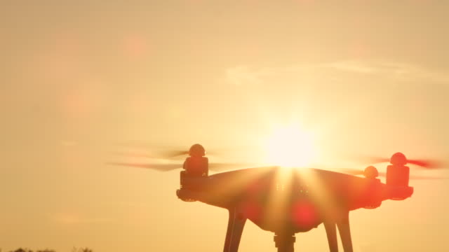 SLOW-MOTION-CLOSE-UP-SILHOUETTE-Filming-Drohne-mit-Kamera-über-goldene-Sonne-fliegen