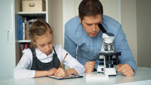 Kleines-Mädchen-mit-Lehrer-im-naturwissenschaftlichen-Unterricht-mit-Mikroskop-auf-dem-Tisch.