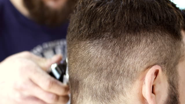 Professionellen-Stylisten-macht-Frisur-mit-elektrischen-Rasierapparat-in-Barbershop-an-client