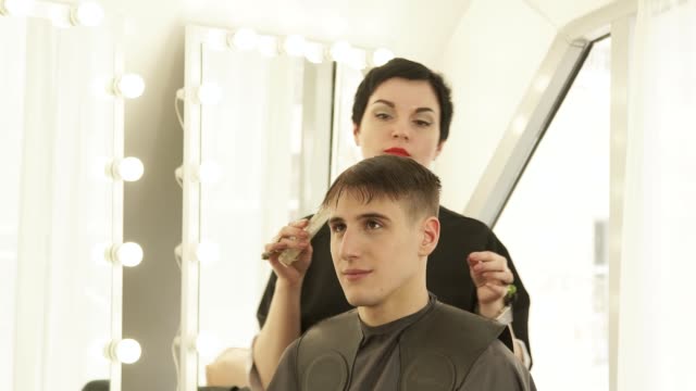 Estilista-mujer-peinando-el-pelo-antes-de-cortar-con-las-tijeras-de-peluquería-en-peluquería.-Haircutter-haciendo-hombre-peinado-con-peine-y-Peluquería-Tijeras-en-estudio-de-belleza