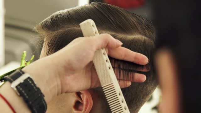 Haircutter-combing-hair-and-cutting-with-hairdressing-scissors-in-beauty-school-close-up.-Hairdresser-doing-male-hairstyle-with-comb-and-hairdressing-scissors-in-barber-shop