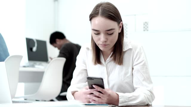 Medium-shot-of-beautiful-female-student-using-her-cell-phone-while-sitting-at-desk-in-computer-class