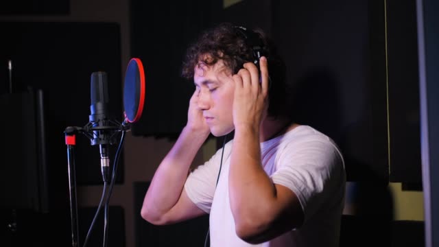 Young-handsome-singer-man-puts-on-headphones-in-the-studio.-Recording-new-melody-or-album.-Male-vocal-artist-with-curly-hair-preparing-for-working.-Slow-motion