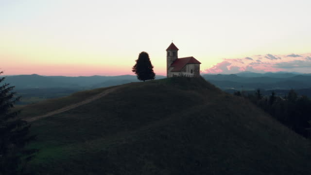 Revealing-shoot-of-a-Catholic-church-on-a-hill-with-a-beautiful-view-to-the-village-in-summertime-in-the-sunset.