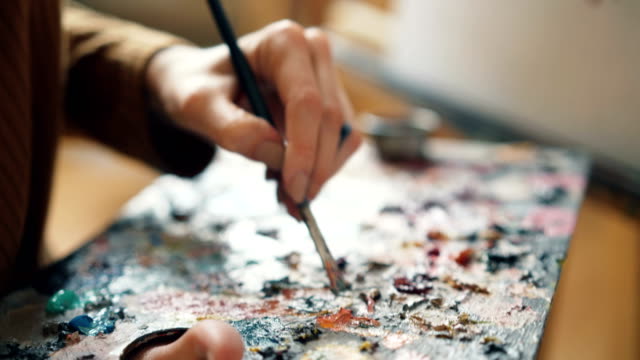 Primer-plano-de-mujer-mano-sujetando-paleta-y-pincel,-mezclar-colores-y-pintar-flores-sobre-lienzo.-Trabajo-artístico,-personas-creativas-y-herramientas-concepto.