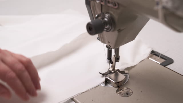 A-closeup-of-a-sewing-machine-stitching-white-fabric.-Female-hands-sewing-it-for-the-wedding-dress