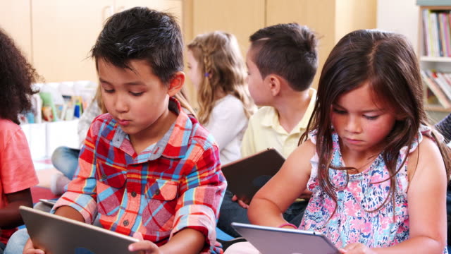 Escuela-primaria-alumnos-sentados-en-el-piso-usando-tabletas