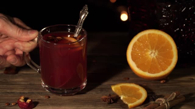 Close-up-of-a-mug-with-mulled-wine.-Male-hand-stir-drink-with-oranges