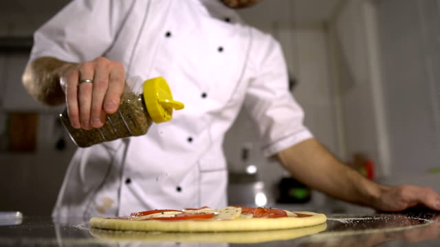 Der-Küchenchef-streut-Gewürze-auf-die-fertige-Pizza-in-der-Küche
