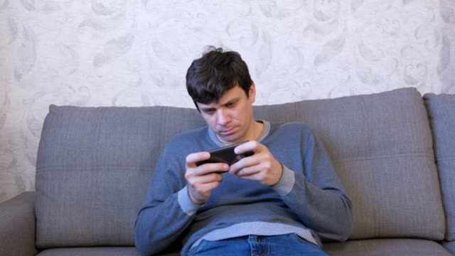 Mann-spielt-Spiel-auf-seinem-Handy-auf-dem-Sofa