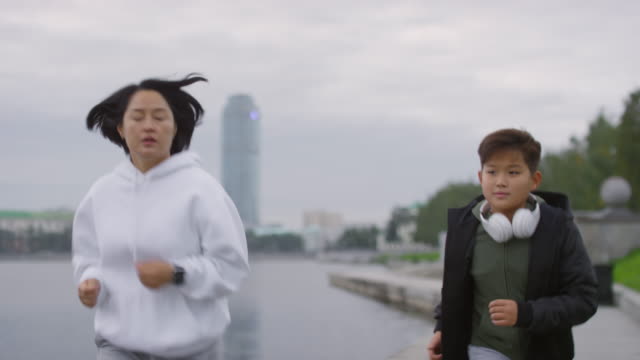 Madre-asiática-e-hijo-corriendo-a-lo-largo-de-Riverside-en-la-ciudad
