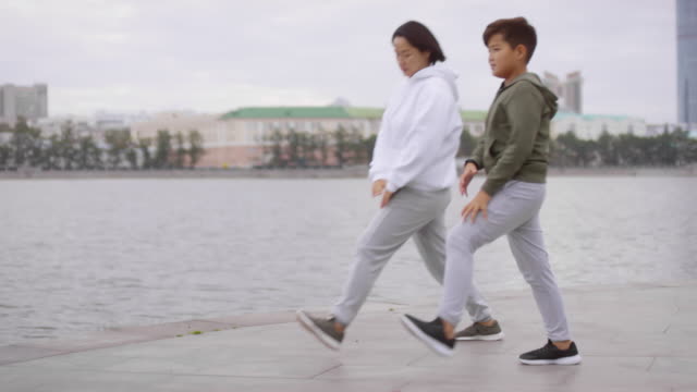 Sportive-Asian-Mother-and-Son-Doing-Lunges-while-Training-on-City-Riverside