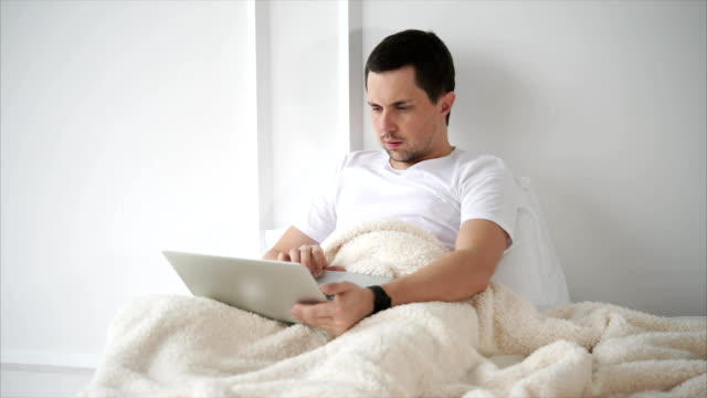 Hombre-navegar-por-web-en-la-computadora-portátil-cuando-está-acostado-en-la-cama