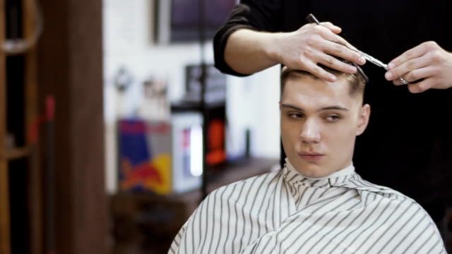 Hairdresser-cuts-hair-of-young-man-in-barbershop