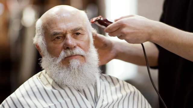 Estilista-hace-peinado-moderno-para-hombre-maduro-con-máquina-de-afeitar-eléctrica