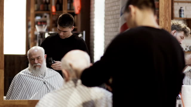 Estilista-profesional-hace-nuevo-peinado-para-madurar-a-hombre-con-máquina-de-afeitar-eléctrica