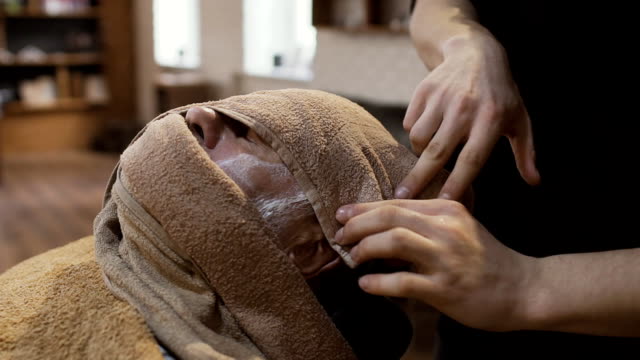 Barber-covers-face-of-senior-man-with-hot-towel-before-shaving