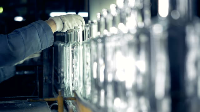 Un-trabajador-de-fábrica-examina-el-cuello-de-las-botellas-sobre-una-cinta-transportadora-en-una-planta.-4K.