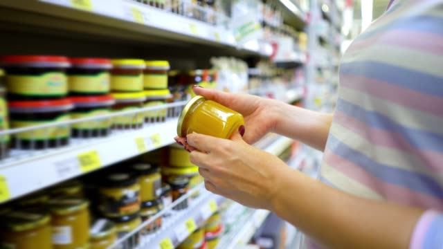 Closeup-caucasian-woman-hands-near-shop-shelves-choosing-light-honey-in-grocery-market