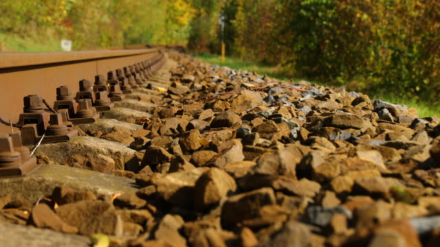 A-close-up-view-of-the-large-screws-securing-the-train-tracks-during-a-sunny-day-with-a-slow-passage-forward-with-a-turn-from-a-side-view-from-below-a-bit-above-the-stones.