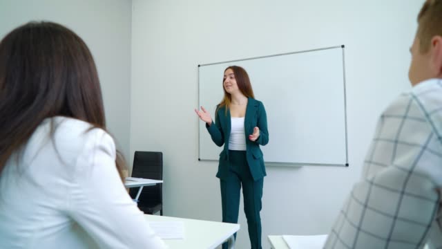 Junge-kaukasischen-Lehrerin-in-der-Nähe-von-Whiteboard-coaching-College-Studenten-im-Klassenzimmer