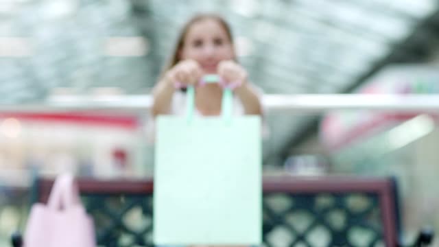 Fade-in-shot-of-young-woman-showing-mint-shopping-bag-in-her-hands-in-mall,-light-pink-polish-on-her-nails