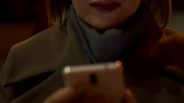 Young-female-reading-smartphone-messages-while-walking-in-night-city,-gadget