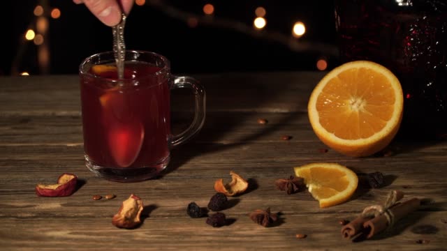 Hand-is-stirring-mulled-wine-standing-on-the-table-with-orange-and-dried-apples