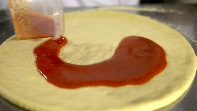 Koch-Hand-breitet-pasteurisierten-Tomatenpaste-auf-einen-Pizzateig-schließen,-sich