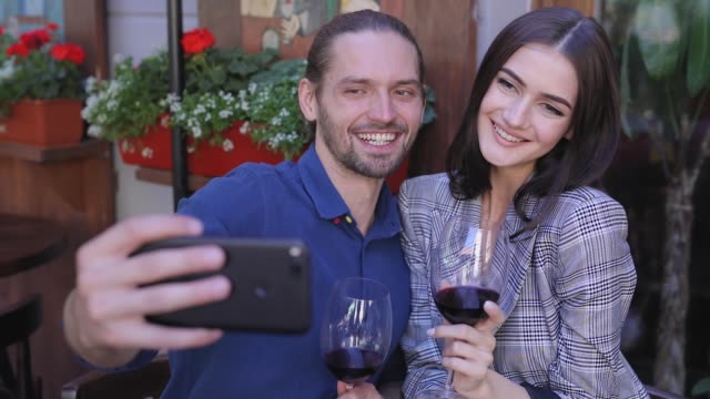 Happy-Couple-With-Wine-Taking-Photos-On-Phone-At-Restaurant