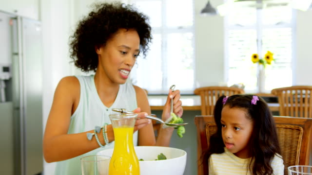 Negro-madre-sirviendo-la-comida-a-su-hija-en-la-mesa-de-comedor-4k