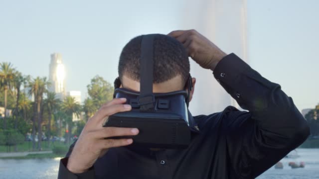 Junge-afrikanische-amerikanische-Mann-mit-VR-Brille-durch-einen-Brunnen-in-einem-Park