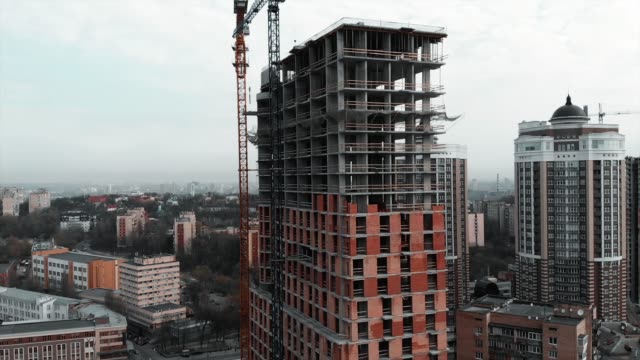 Construction-crane-at-construction-site.-Construction-of-brick-concrete-residential-building,-aerial-drone-view.-Unfinished-high-rise-house