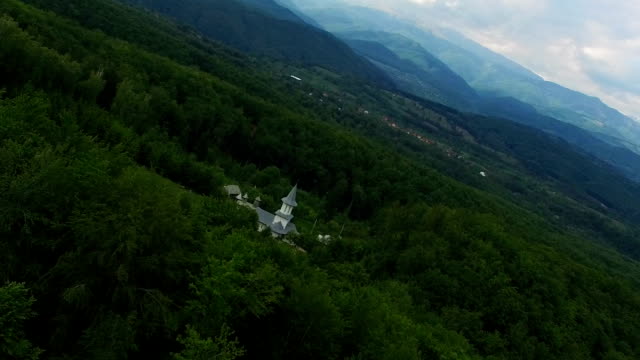 Christian-church-surrounded-by-green-forest,-aerial-flight,-Ciocanu-Monastery,-Romania