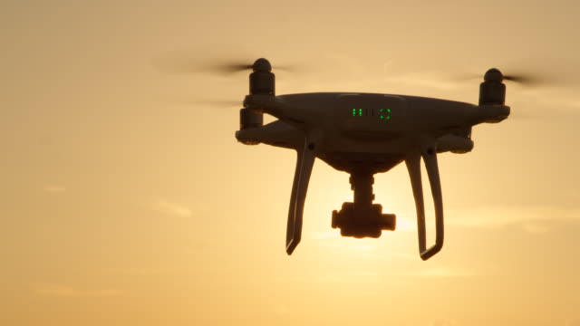 SLOW-MOTION-CLOSE-UP-SILHOUETTE:-Drone-flying-towards-the-sun-at-golden-sunset